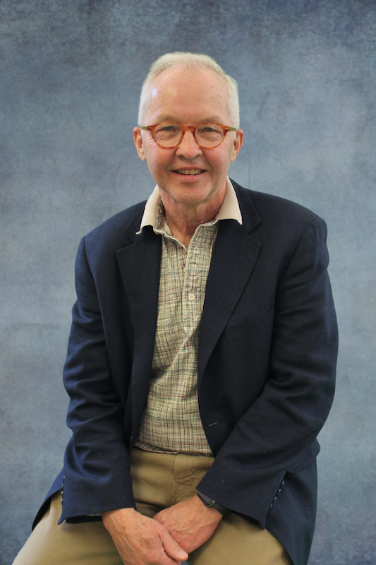 Man in dark suit jacket in front of gray background.