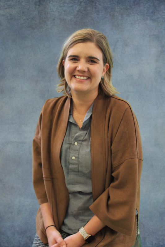 Woman in brown cardigan in front of gray background.