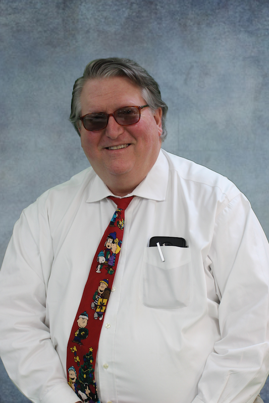 Man in white shirt and red tie in front of gray background.