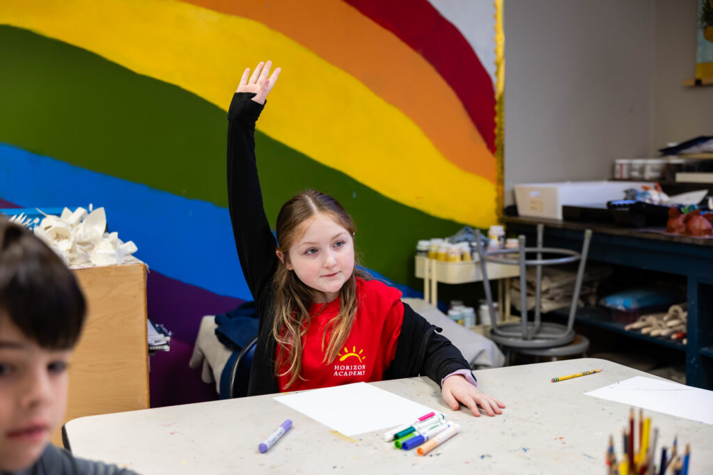 Student completing a classroom assignment in front of a colorful classroom mural at Horizon Academy.