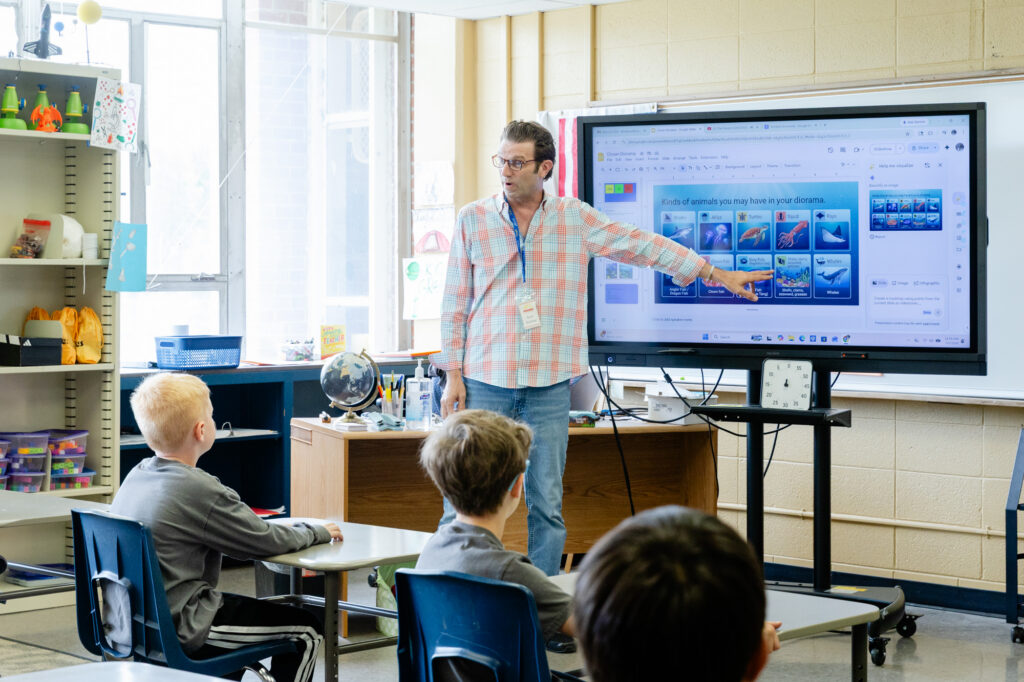 Teacher presenting a lesson to lower school students using an interactive display.