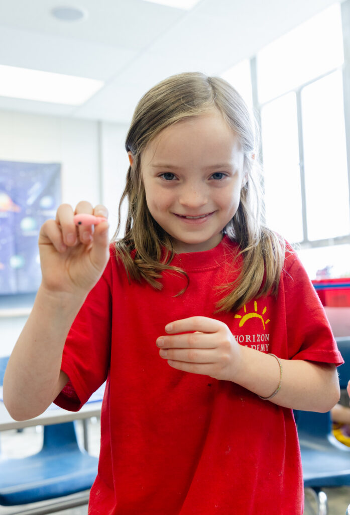 Lower school student proudly showing a completed classroom project.