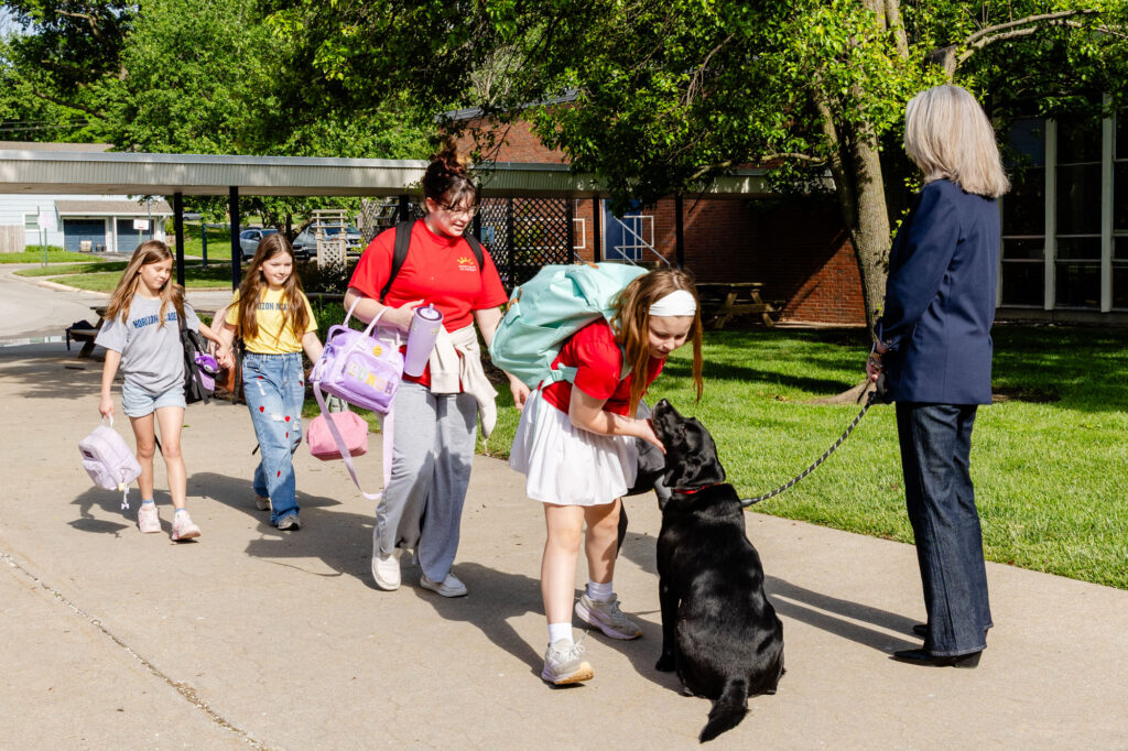 Students and staff walking outdoors with a service dog during a morning meeting at Horizon Academy.