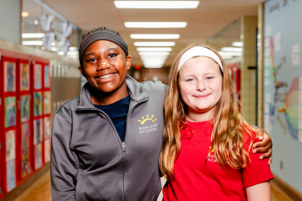 Two students smiling together in a hallway at Horizon Academy.