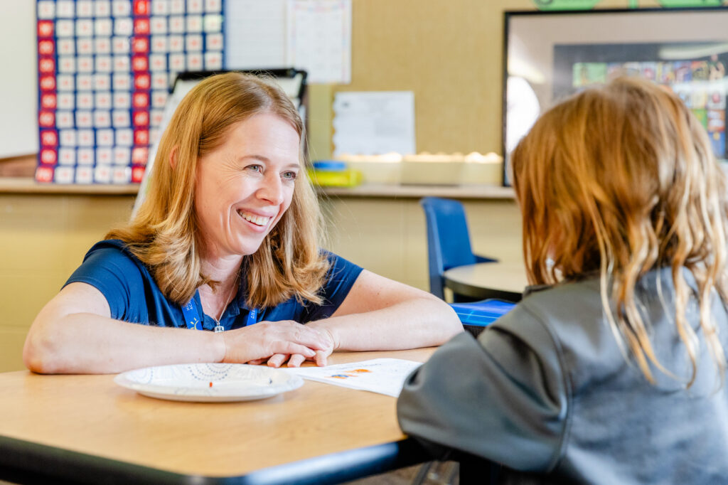 Occupational therapist working one-on-one with a student at a classroom table.