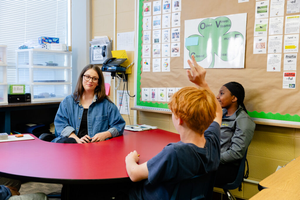 Educator meeting with students around a table during a collaborative learning session.