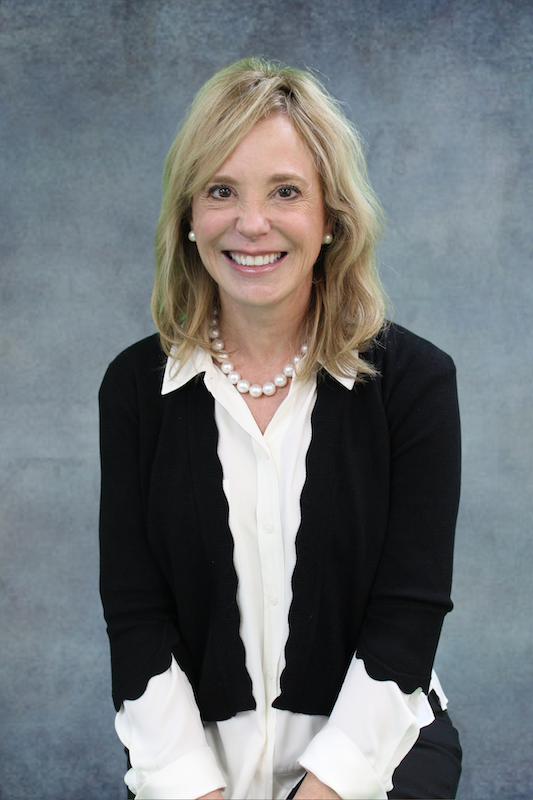 Woman in dark jacket in front of gray background.