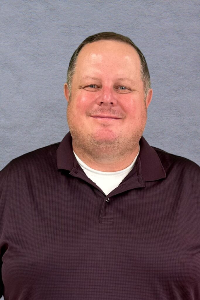 Man in dark polo shirt in front of gray background.