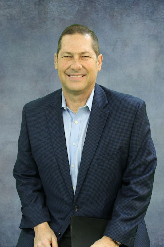 Man in blue suit jacket in front of gray background.