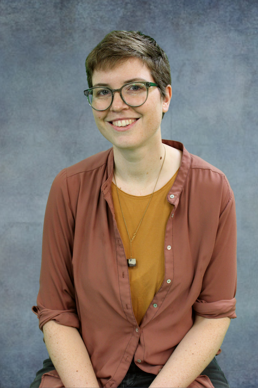 Person wearing a brown button shirt over an orange shirt in front of gray background.
