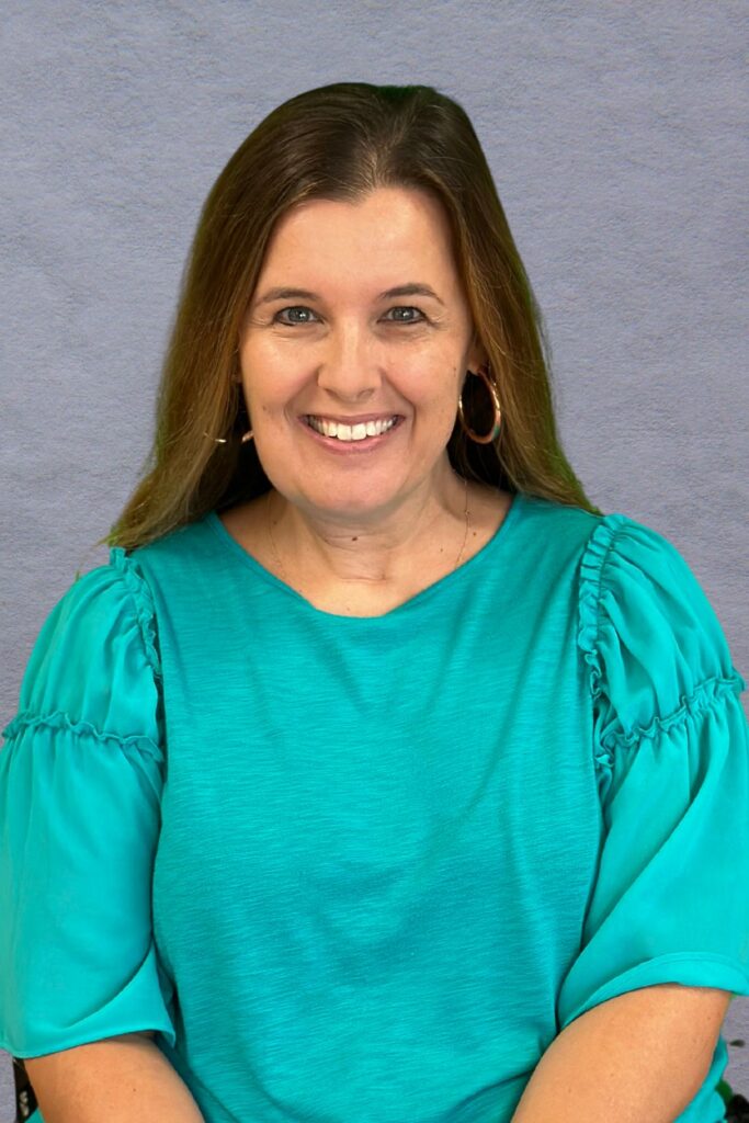 Woman in blue shirt in front of gray background.