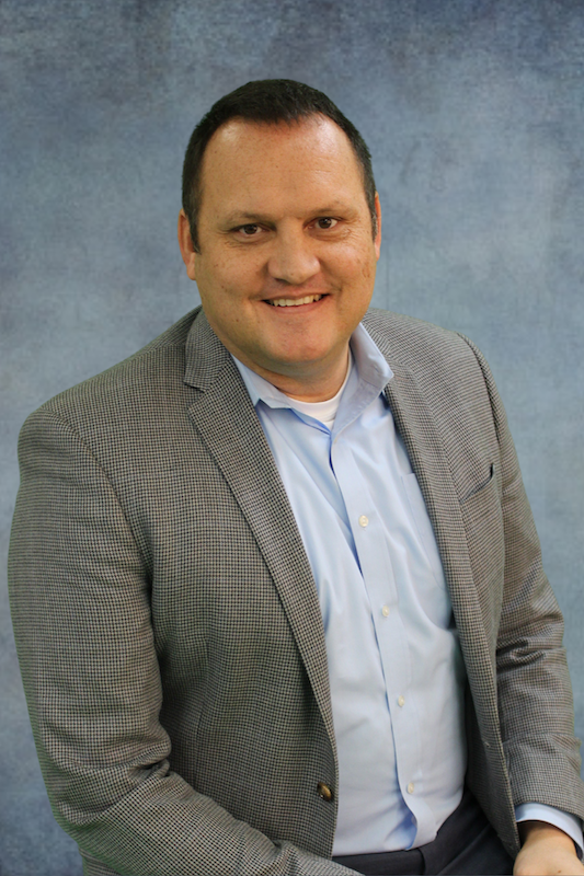 Man in brown suit jacket in front of gray background