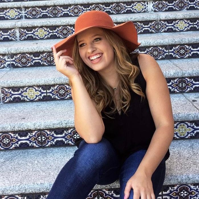 Person in an orange hat smiling while sitting on a decorative staircase.