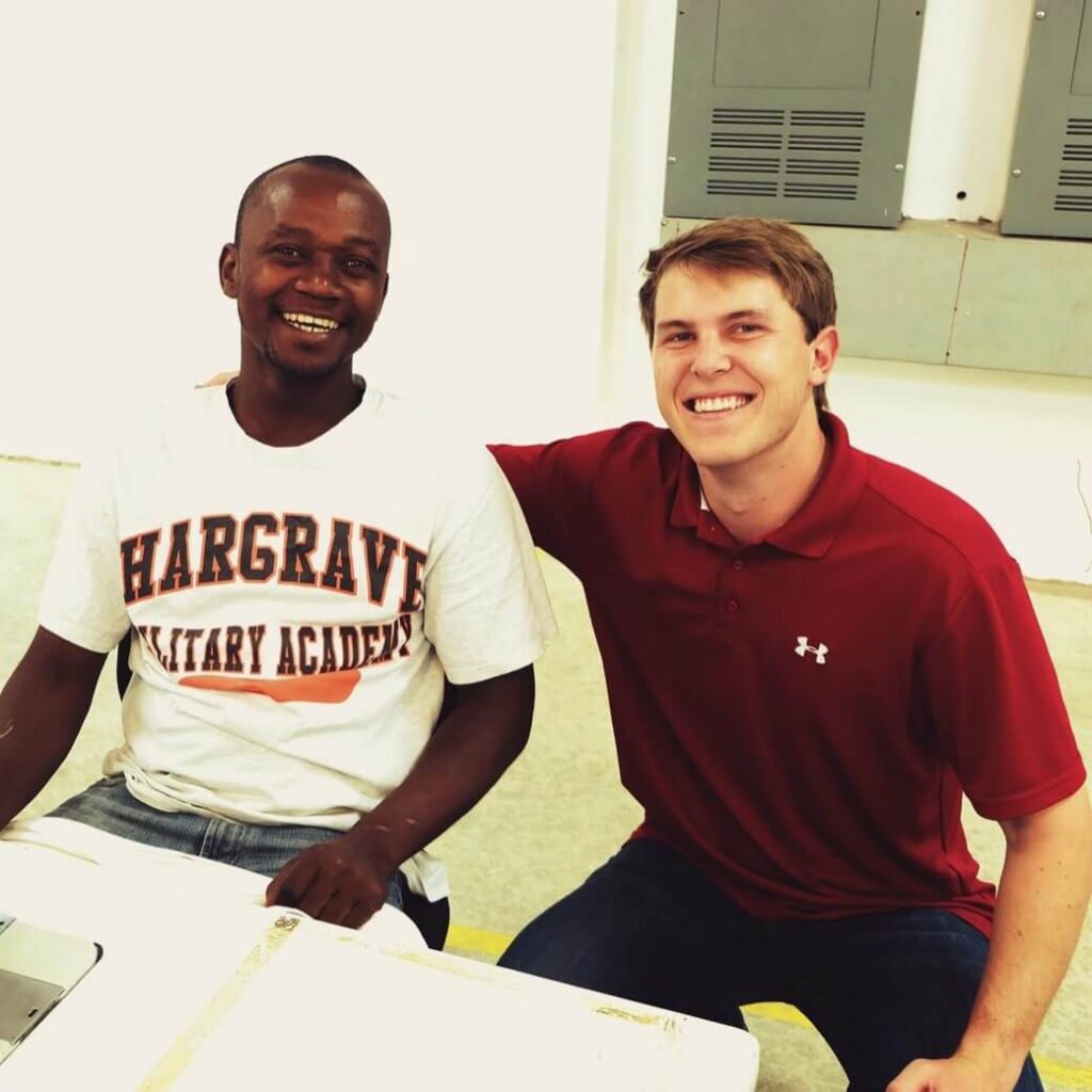 Two young men, one wearing a white academy shirt and the other in a red polo, smiling for the camera.