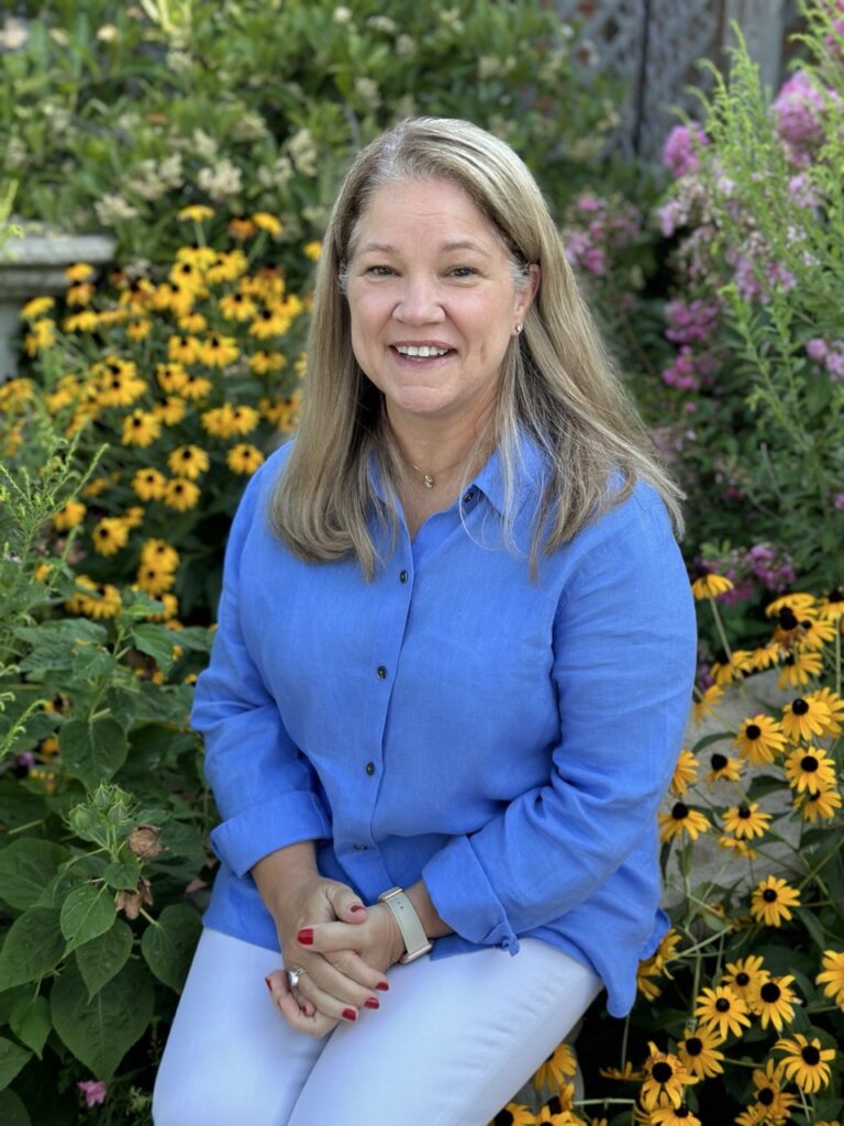 Staff member seated outdoors wearing a blue shirt in front of flowers at Horizon Academy.