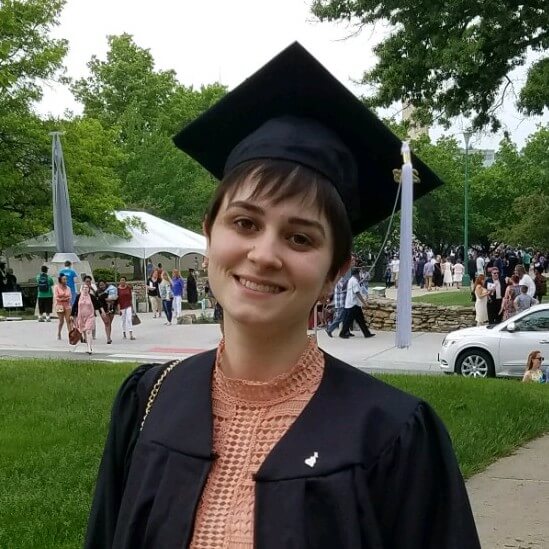 Recent graduate in black cap and gown. smiling outside.