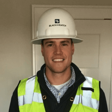 Person smiling while wearing a white hardhat and a yellow safety vest.