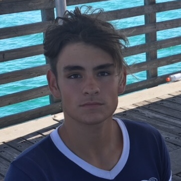 Person looking into the camera while standing on a dock by a body of water.