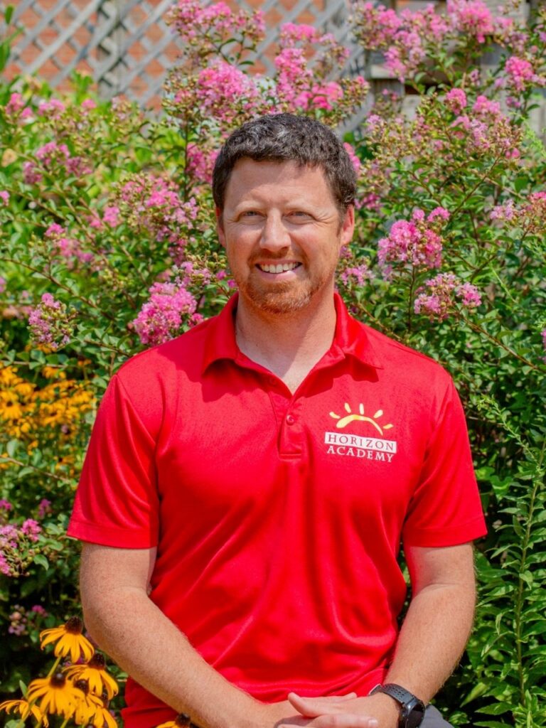 Staff member pictured in front of flower bushes on the Horizon Academy campus.