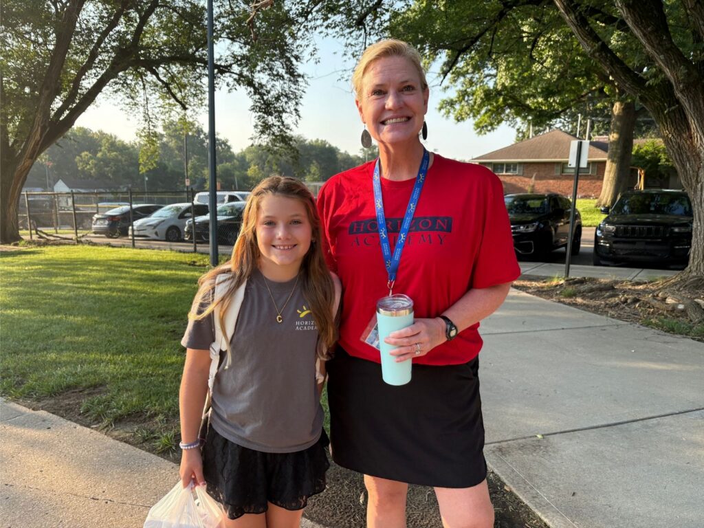 The principal celebrating Dyslexia Awareness Month in a red shirt while standing beside a schoolgirl with a backpack on a sidewalk.